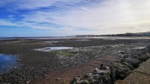 A coastal landscape with rocky terrain, a body of water, and distant buildings. - Perfect for couples and familes to come and enjoy the local area. (Minehead)