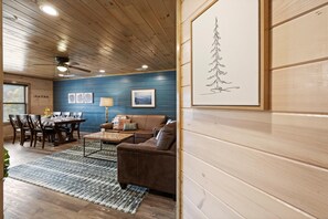 Un salon chaleureux avec un plafond en bois, un canapé en cuir marron, une table à manger avec des chaises et des œuvres d’art encadrées accrochées aux murs.