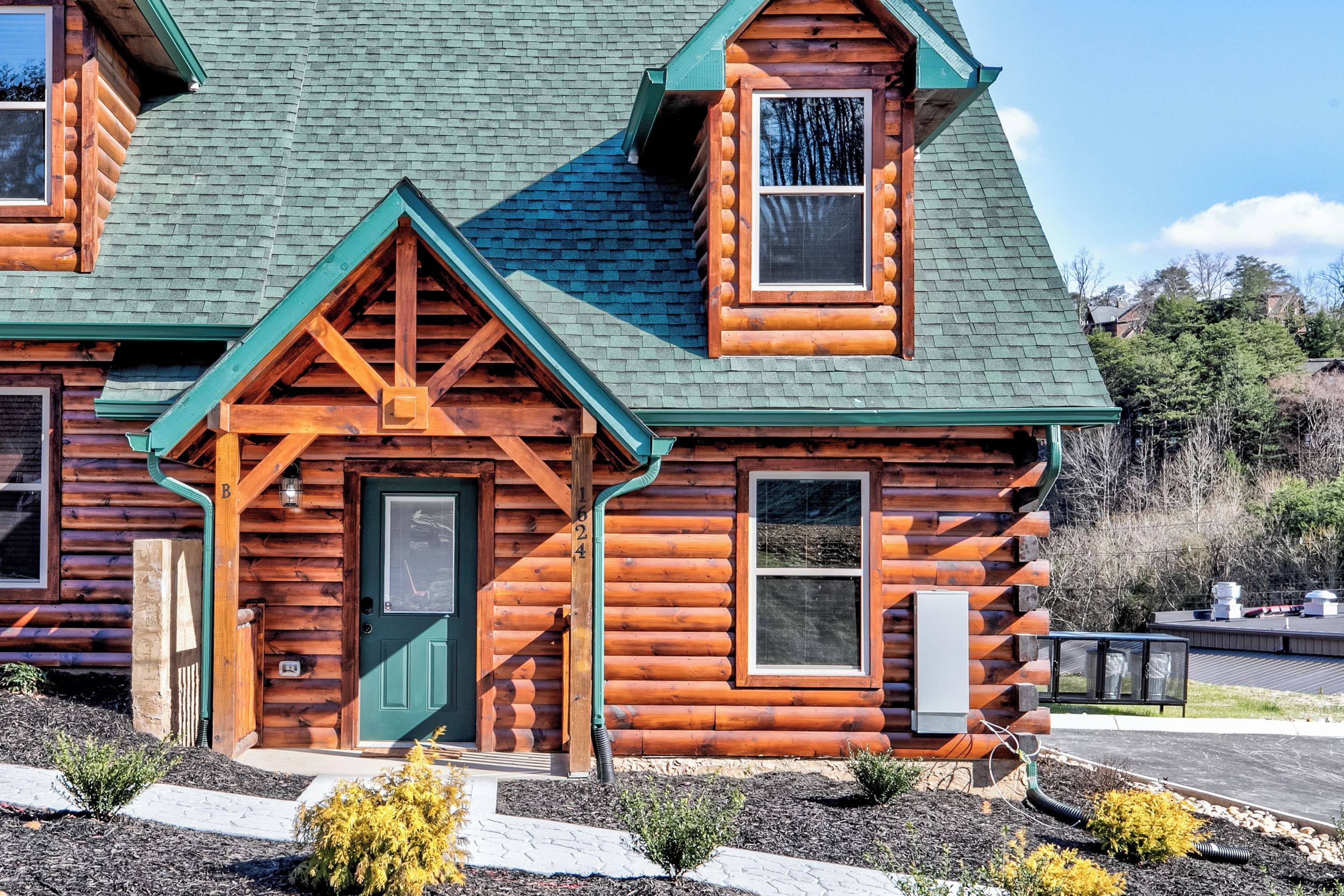 A log cabin with a green roof, a front porch, and a visible number '1624' on the door.
