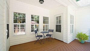 A covered porch with white siding, a wooden deck, and a table with two chairs. - Fenced yard close to downtown Wake Forest and 20 min to Raleigh (Wake Forest)