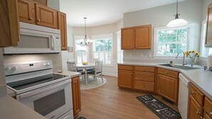 A kitchen with wooden cabinets, a white stove, a microwave, and a dining area with a table and chairs. - Fenced yard close to downtown Wake Forest and 20 min to Raleigh (Wake Forest)
