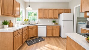 A modern kitchen with wooden cabinets, a white refrigerator, and a window providing natural light. - Private Wooded Retreat | Fenced Yard | Near Downtown (Wake Forest)