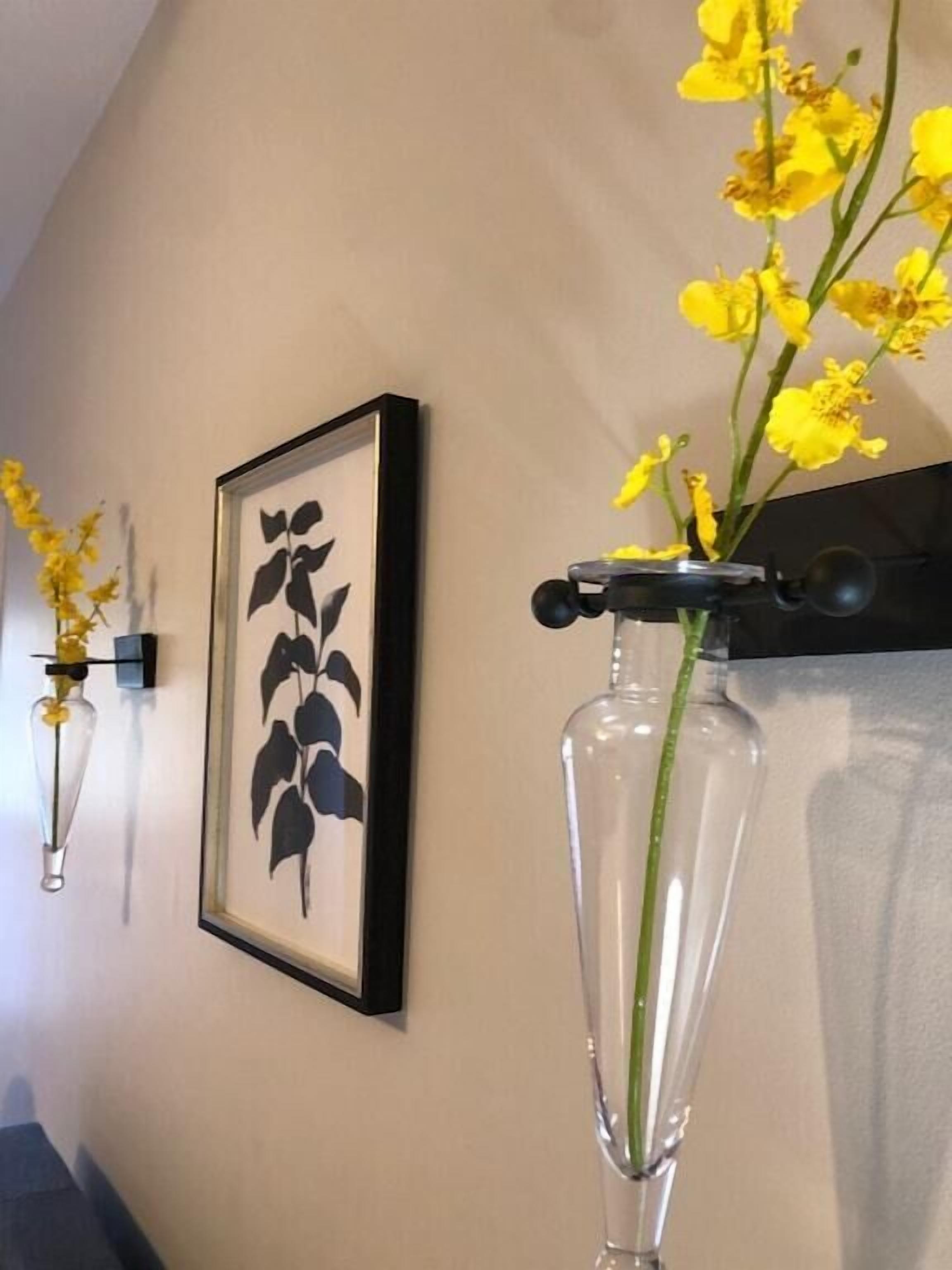 Un mur orné de deux reproductions botaniques encadrées et d’un vase transparent contenant des fleurs jaunes.