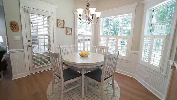 A dining area with a round table, white chairs, a chandelier, and large windows with shutters. - Fenced yard close to downtown Wake Forest and 20 min to Raleigh (Wake Forest)