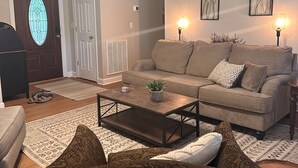 A living room with a sofa, coffee table, patterned rug, and a door with a stained glass design. - Fenced yard close to downtown Wake Forest and 20 min to Raleigh (Wake Forest)