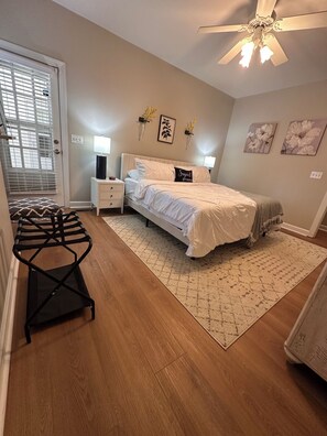 A bedroom with a bed, bedside tables, a ceiling fan, and a window with blinds. - Private Wooded Retreat | Fenced Yard | Near Downtown (Wake Forest)