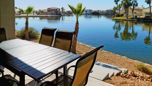 An outdoor patio with a table and chairs overlooking a calm lake, surrounded by palm trees and residential buildings. - Gorgeous 5-Star Home on the Lake, near Laughlin/Bullhead Casinos & Lake Mohave (Bullhead City)