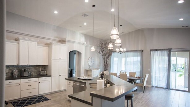 A modern kitchen with white cabinetry, a central island, pendant lighting, and a dining area with a view. - Gorgeous 5-Star Home on the Lake, near Laughlin/Bullhead Casinos & Lake Mohave (Bullhead City)