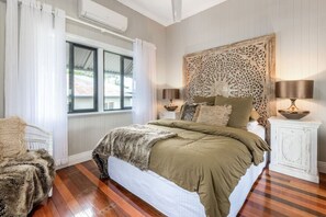 Ein Schlafzimmer mit einem großen Bett, einem dekorativen Kopfteil, zwei Nachttischen mit Lampen und einem Fenster mit Vorhängen.