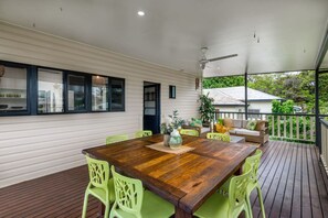 A covered outdoor dining area with a wooden table and green chairs, a ceiling fan, and a view of greenery outside. - `Kookaburra` at Savannah House (Westcourt)