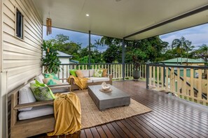 A covered outdoor deck with a sofa, coffee table, and a view of the surrounding greenery.