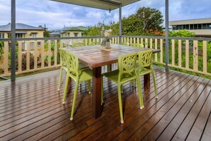 Eine Holzterrasse mit Tisch und Stühlen, umgeben von einem weißen Zaun und viel Grün.