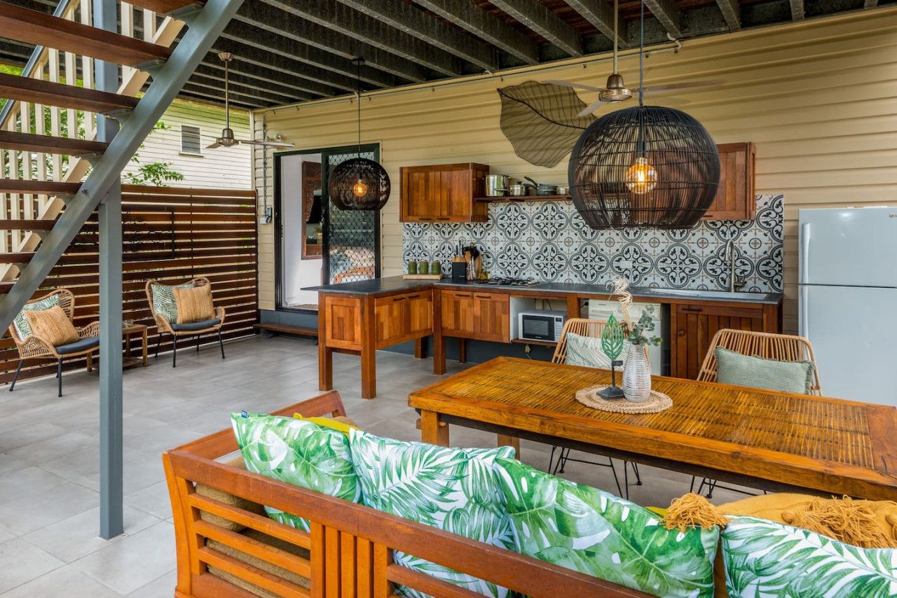A kitchen with a dining area, featuring wooden cabinets, a patterned backsplash, and a large hanging light fixture.