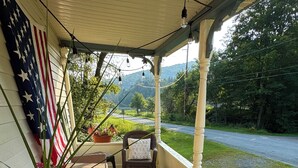 A porch with wicker chairs, a wooden barrel planter with flowers, and an American flag.