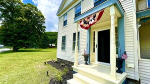 A two-story house with a front porch, a flag, and a well-maintained lawn.