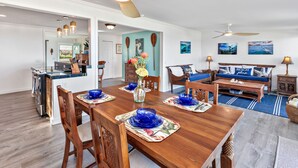 A spacious living area with a wooden dining table, blue chairs, and a sofa with a 'BEACH please' sign. - Oceanfront Mokuleia Home with Stunning Views (Waialua)