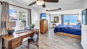 A bedroom with a bed, a desk, a chair, a ceiling fan, and a TV. - Oceanfront Mokuleia Home with Stunning Views (Waialua)