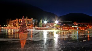 Een nachtzicht van een stad met een grote, verlichte kerstboom op de voorgrond, weerspiegeld in een bevroren wateroppervlak.