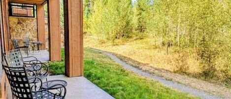 A covered patio with outdoor seating and a view of a forested area.