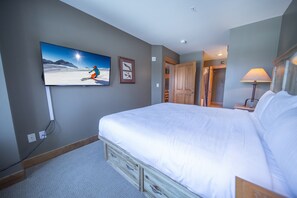 A bedroom with a large bed, a television mounted on the wall, a wooden wardrobe, and a lamp on the side table. - Springs 8843 (Keystone)