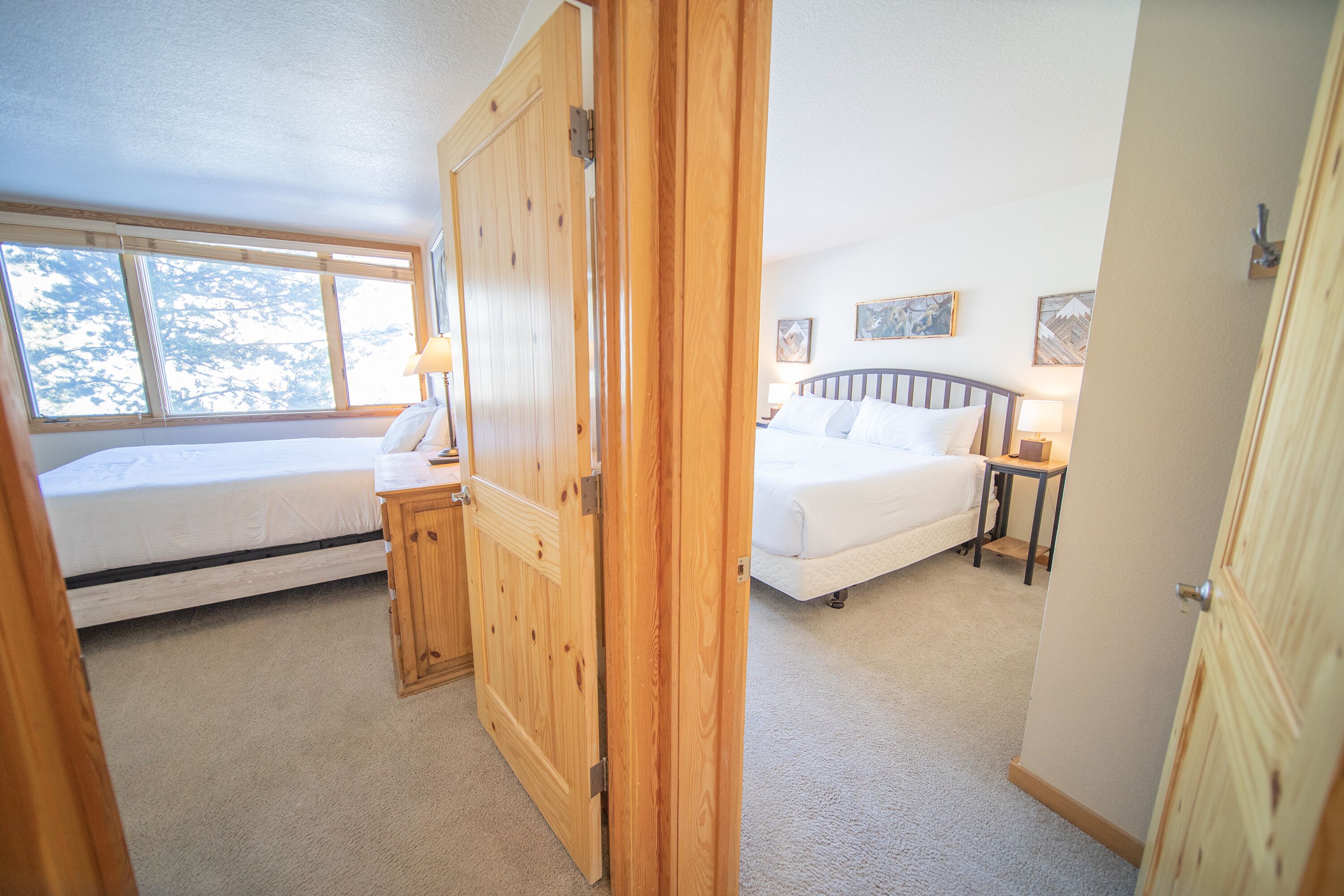 Une chambre avec deux lits, des portes en bois et une vue sur les arbres par la fenêtre.