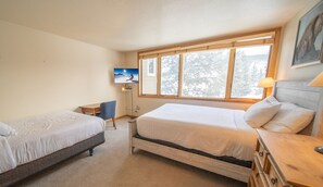 A hotel room with two beds, a desk, a chair, a TV, and a window with a view of trees. - Pines 2167 (Keystone)