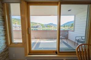 Una habitación con puerta corrediza de vidrio que da a un balcón con vista a un lago y montañas.