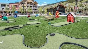 Een midgetgolfbaan met een rode schuur, picknicktafels en een speelplaats.