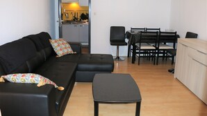 Un salon avec un canapé noir, un pouf assorti et un coin repas comprenant une table et des chaises.