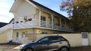 Un immeuble de deux étages doté d’un balcon, d’un escalier et d’une voiture garée.