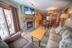 A living room with a fireplace, a sofa, a coffee table, and a dining area with chairs. - Red Hawk Lodge 2281 (Keystone)