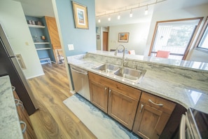 A kitchen with wooden cabinets, a marble countertop, and a stainless steel sink.