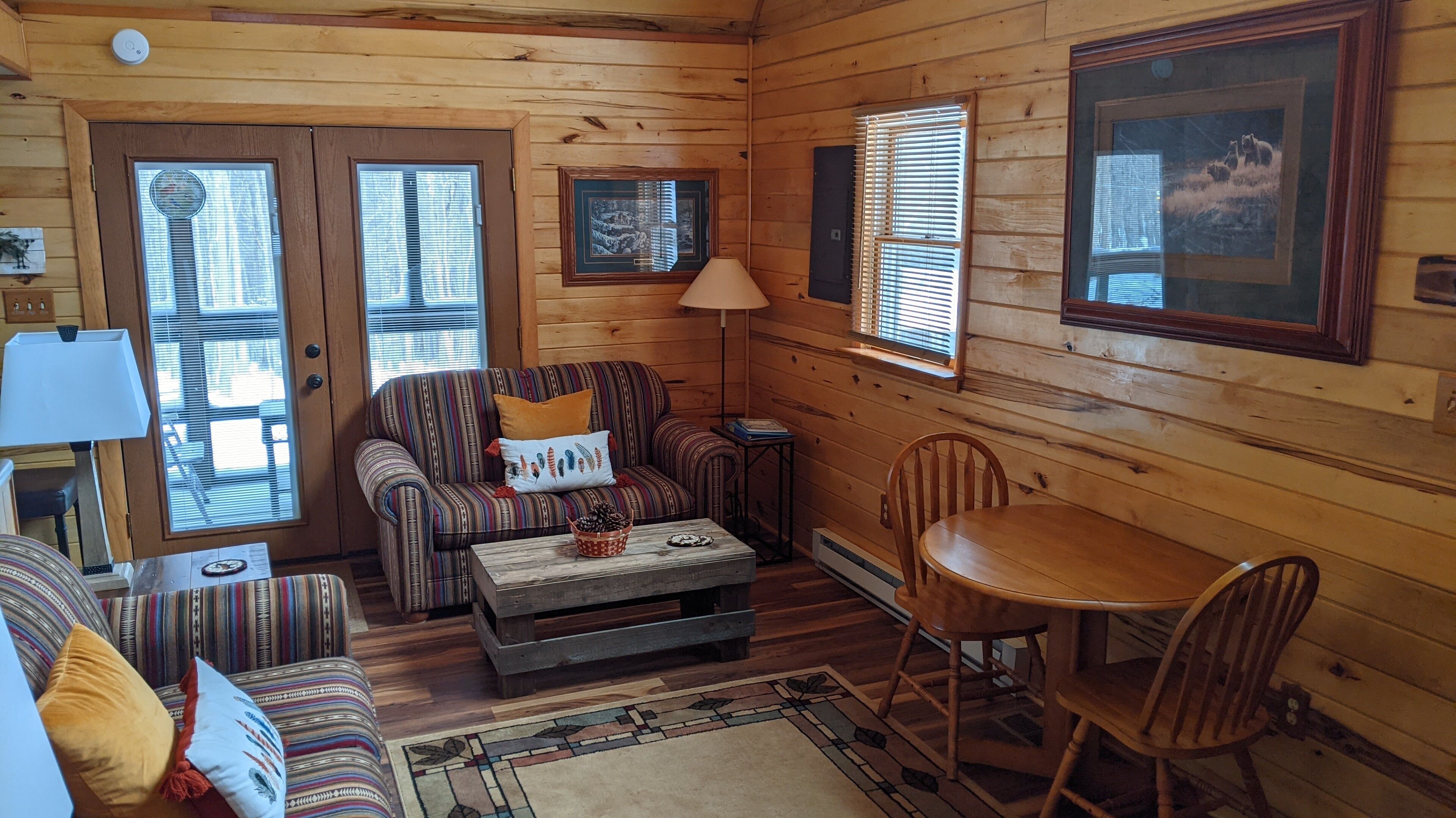 A cozy cabin interior with a striped sofa, a wooden dining table, and a fireplace.