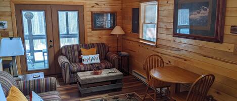 A cozy cabin interior with a striped sofa, a wooden dining table, and a fireplace.