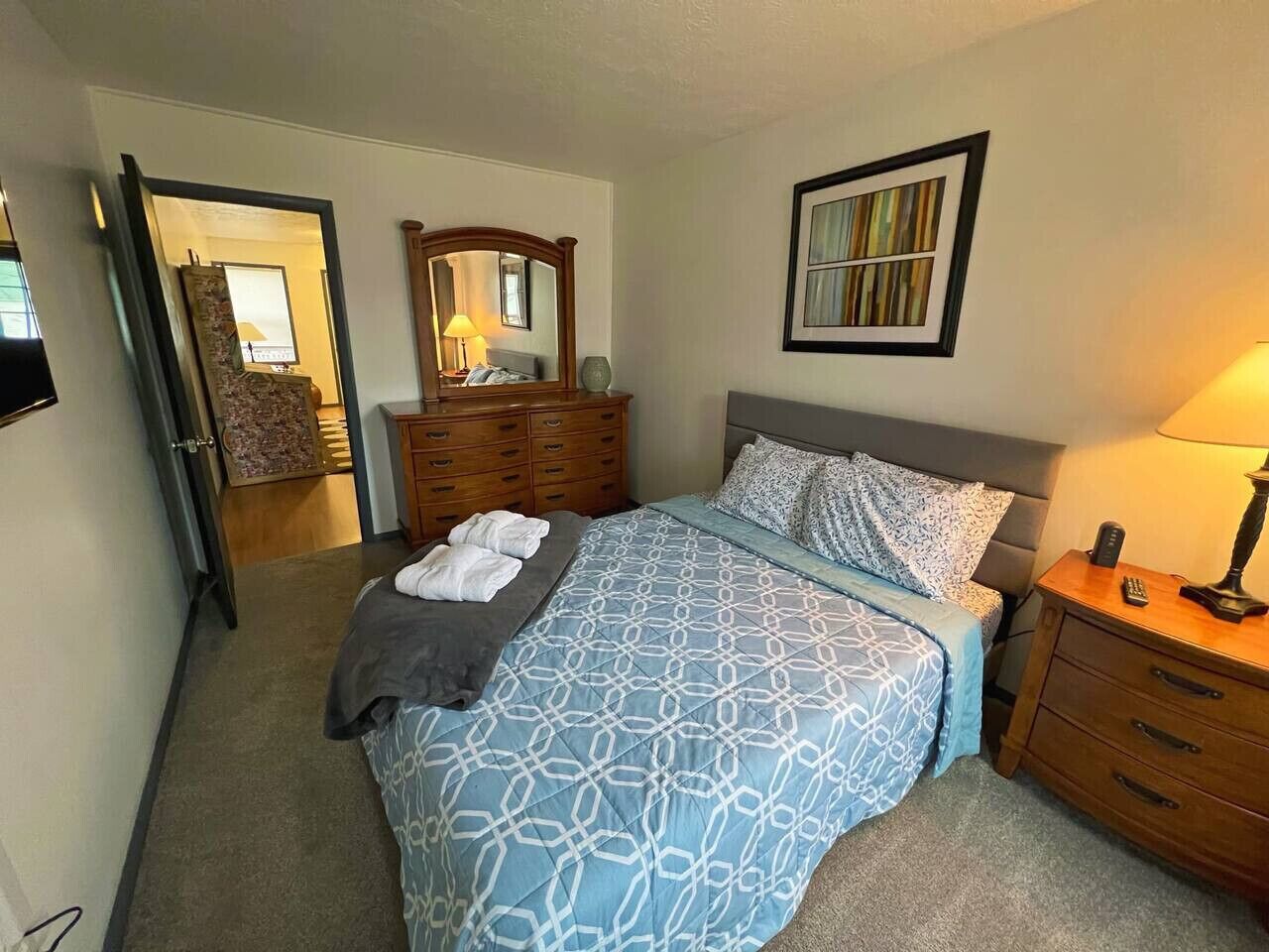 A bedroom with a bed, bedside tables, a dresser, a mirror, and a framed picture on the wall.