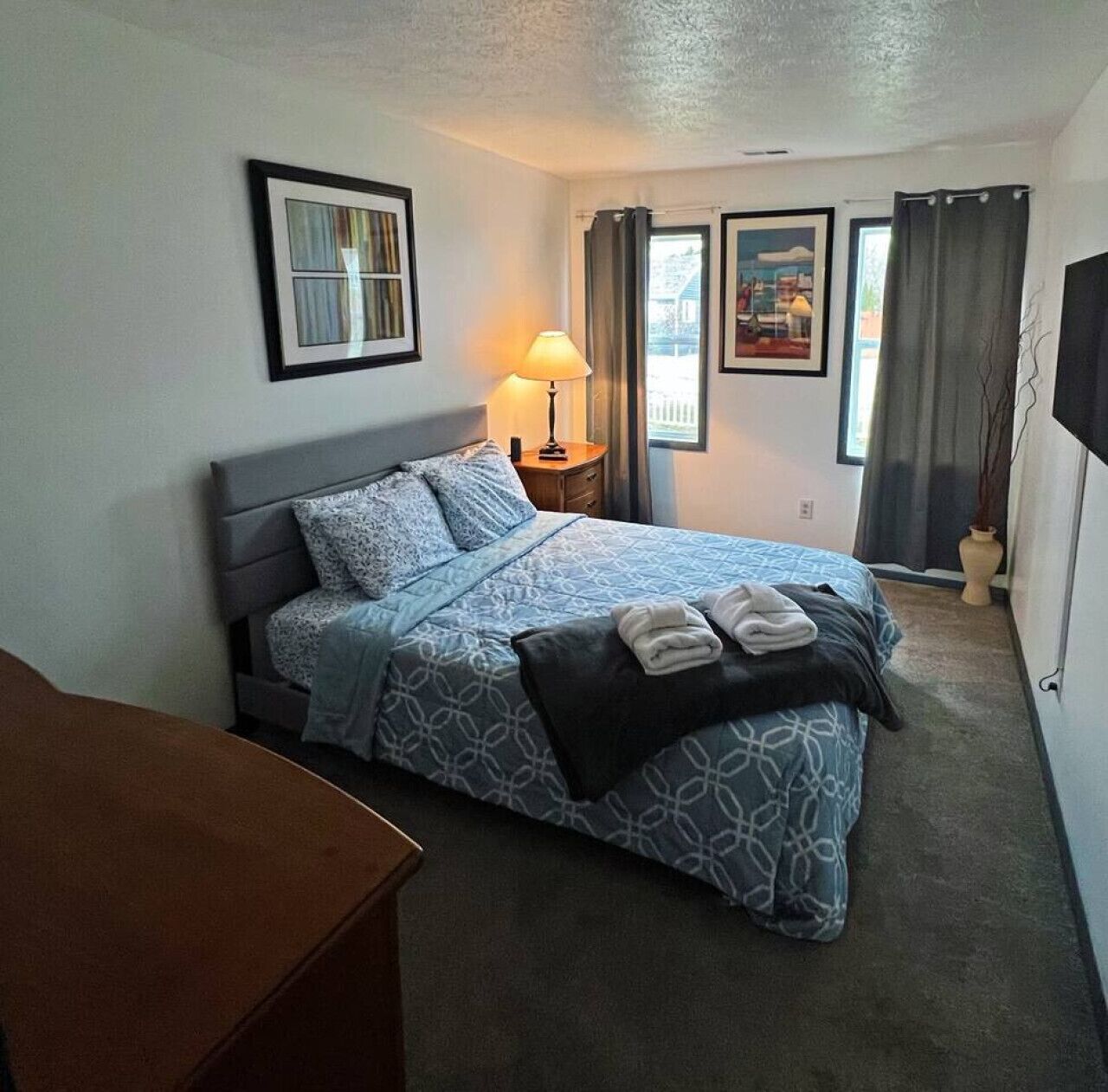 Una camera da letto ordinata con un letto, un comodino, una lampada e quadri appesi al muro.