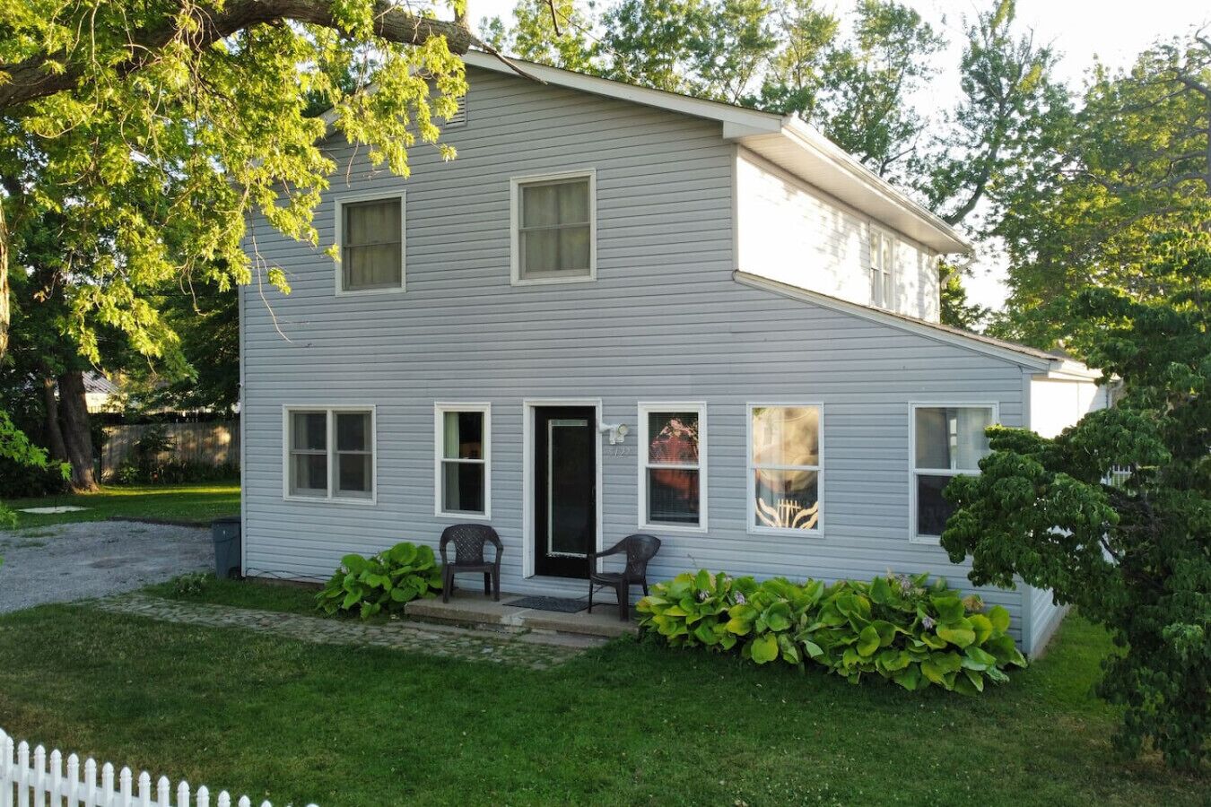 A two-story house with a front porch, a small garden, and a white picket fence.