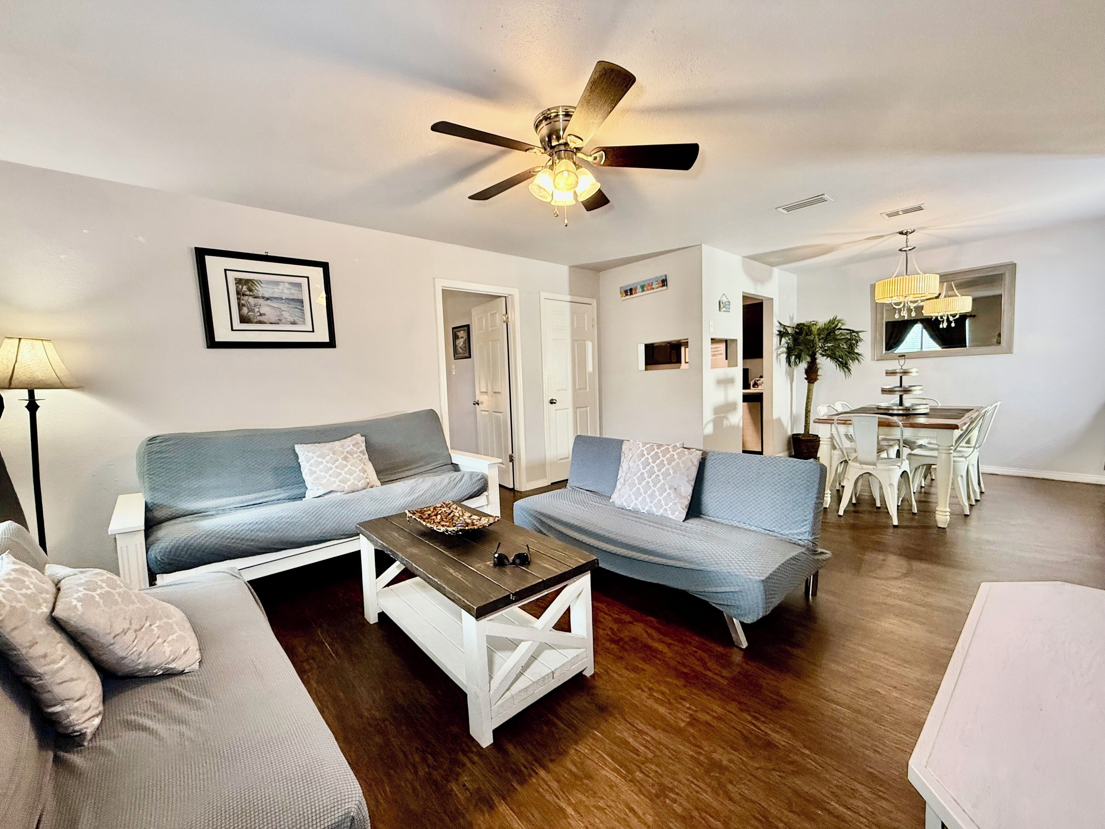 A modern living room with a grey sofa, a wooden coffee table, and a dining area with a white table and chairs.