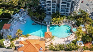 A resort with a large central pool, multiple balconies, and a beach area.