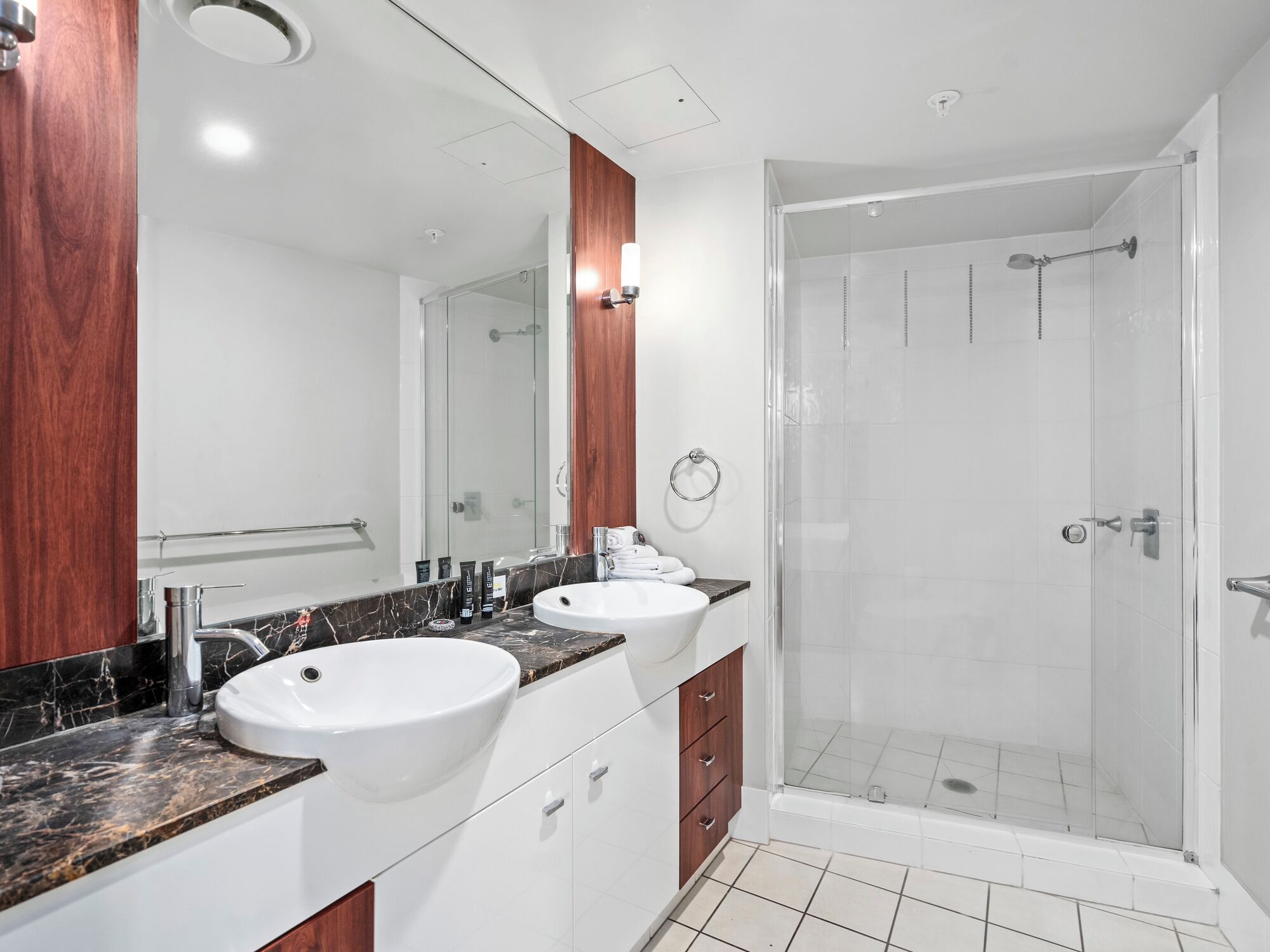 A modern bathroom with two sinks, a glass shower enclosure, and a wooden vanity.