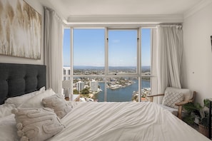 Une chambre avec un grand lit, une vue sur la ville et l’eau, et un panorama de la ligne d’horizon urbaine visible par la fenêtre.
