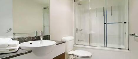 Un baño con lavamanos blanco, inodoro y ducha con mampara de vidrio.