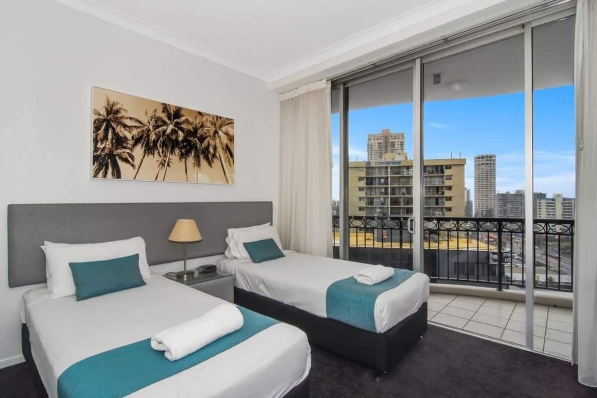 Ett hotellrum med två sängar, ett stort fönster med utsikt över staden och en tavla med ett palmträd på väggen.