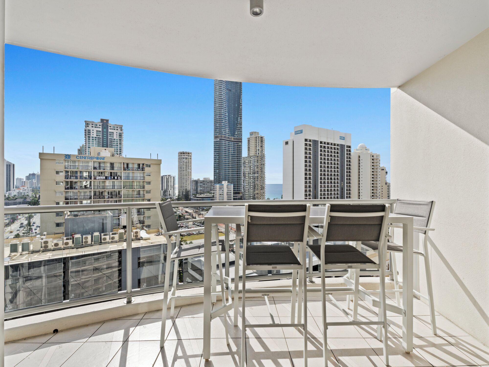 A balcony with a table and chairs, overlooking a cityscape with various buildings.