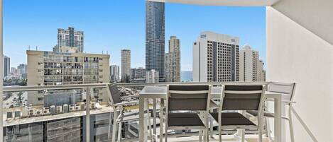 A balcony with a table and chairs, overlooking a cityscape with various buildings.