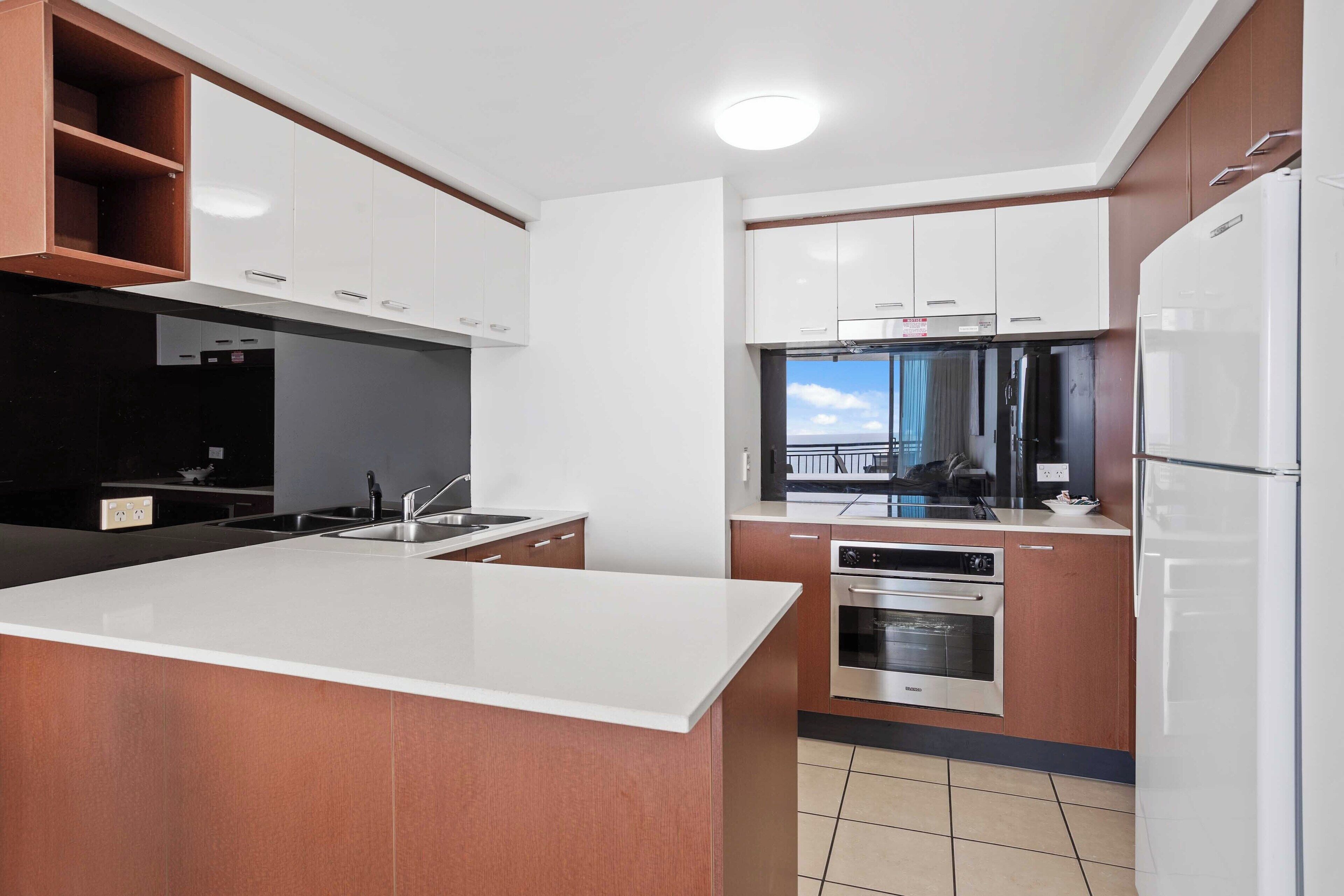 A modern kitchen with white cabinets, a central island, stainless steel appliances, and a view of the outdoors.