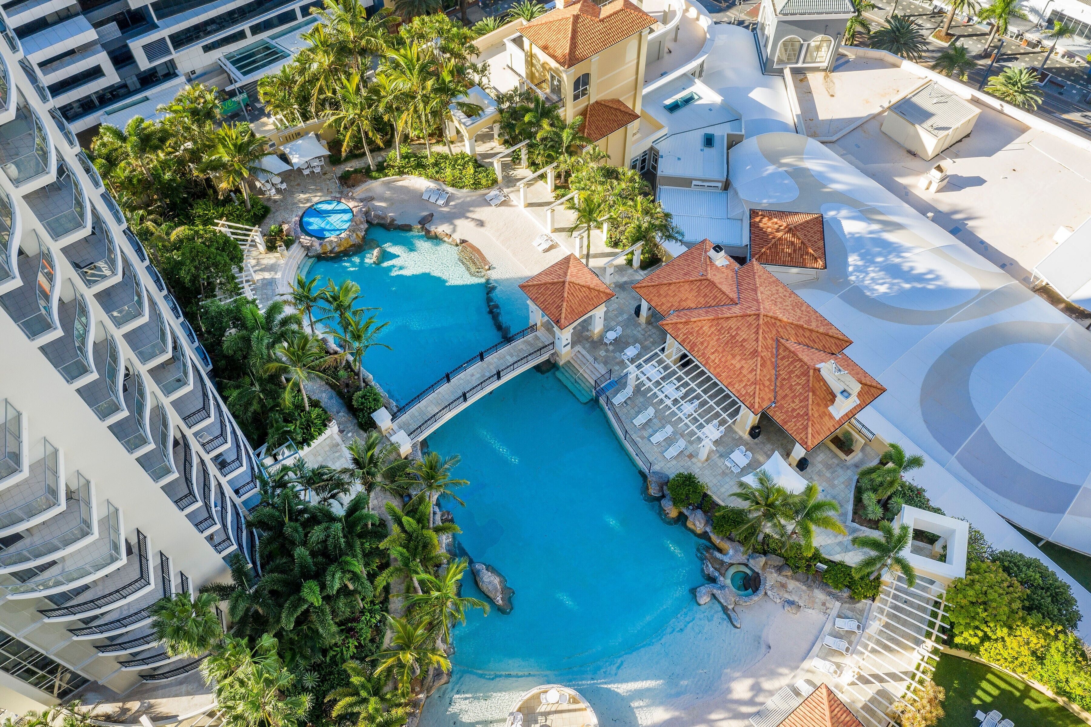 A resort with a large swimming pool, palm trees, and a modern building with balconies.