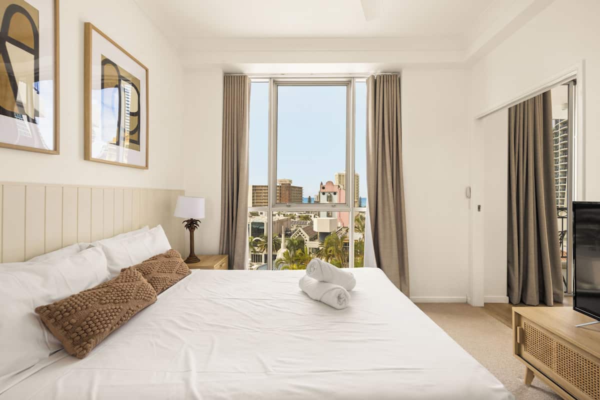 Ett hotellrum med en stor säng, en tv och utsikt över byggnader genom fönstret.