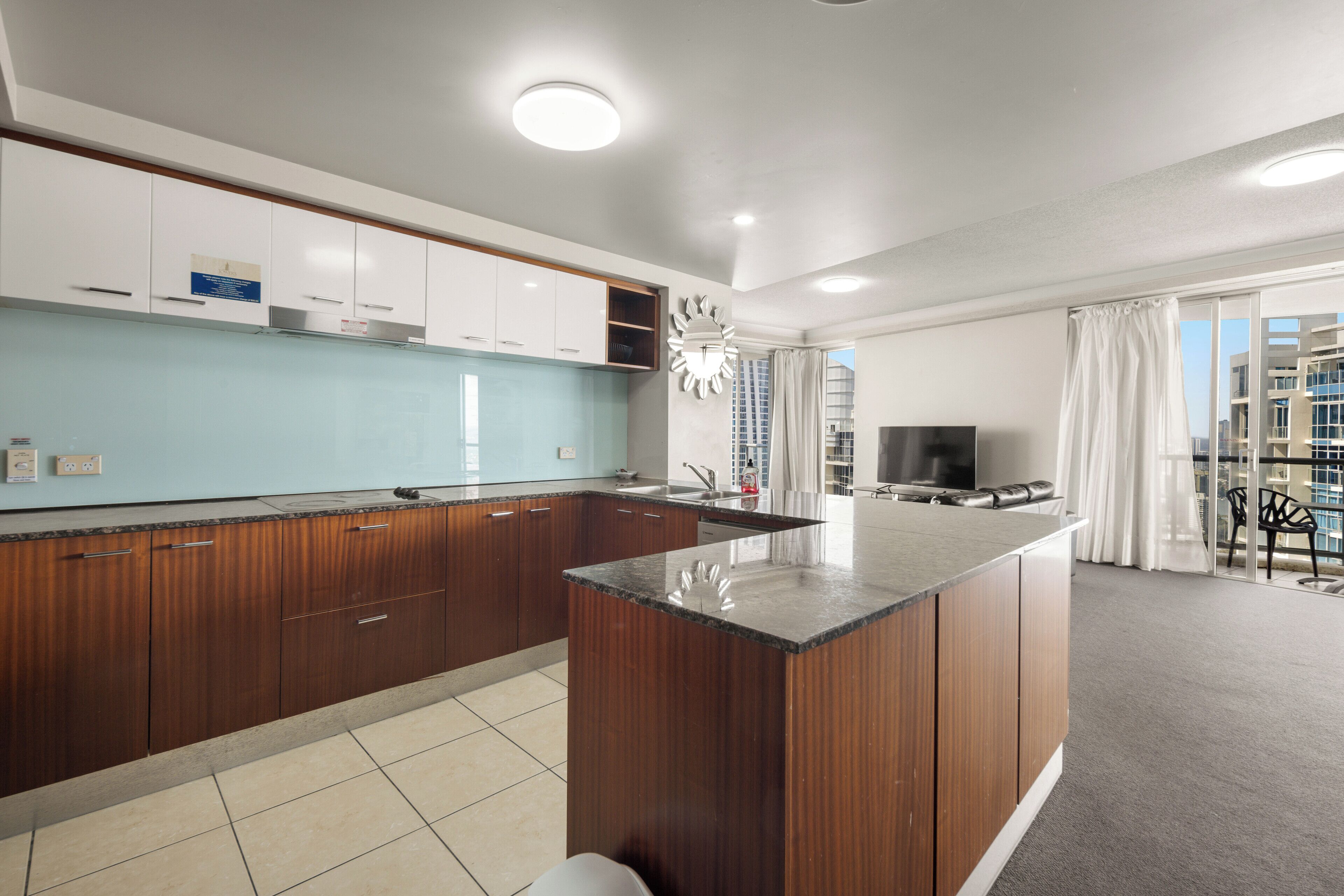 A modern kitchen with wooden cabinets, a central island, and a dining area with a TV and chairs.