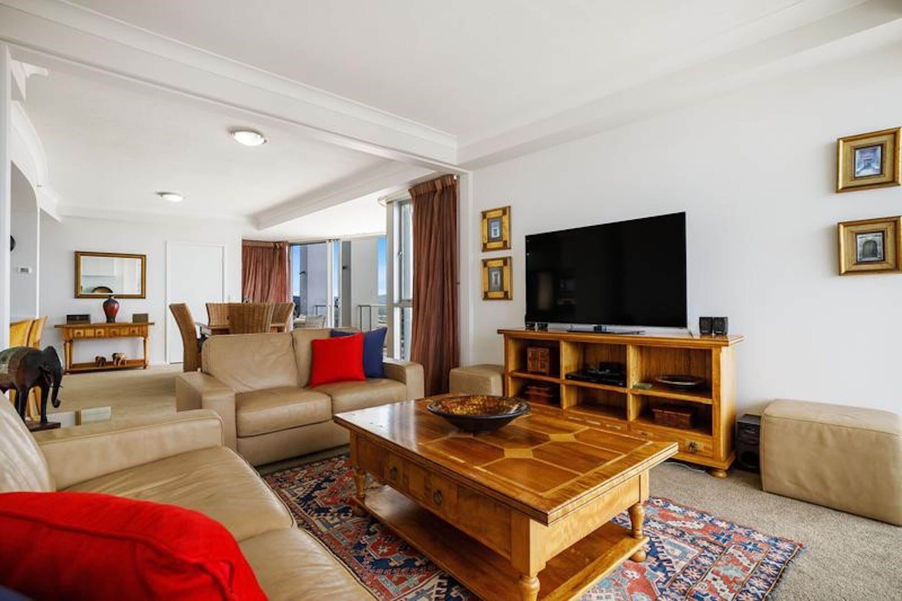 Un salon spacieux avec un grand téléviseur à écran plat, une table basse en bois et un canapé beige.